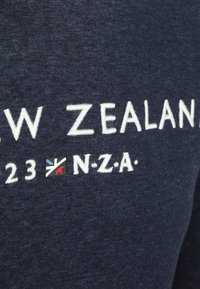 Marineblauwe sweatshirt met witte geborduurde tekst "NIEUW-ZEELAND" en een klein logo met rode, blauwe en witte details. Zachte textuur.