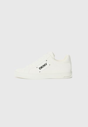 Hvite lerrets sneakers med lav profil, med en svart DKNY-logo på siden, rund tå, snøring foran og glatt tekstur.