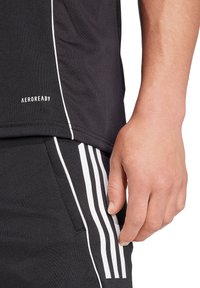 Zwart sportshirt met wit AEROREADY-logo. Heeft een ronde halslijn en een soepele textuur. Zwarte broek met drie witte verticale strepen.