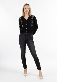 Cardigan negru cu decolteu în V, cu nasturi în față și motive decorative cu inimi aurii. Asociat cu blugi închis la culoare și pantofi cu toc bej. Simplu și funcțional.
