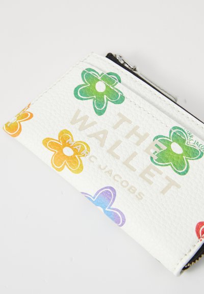 Balts ādas maks ar krāsainiem ziedu rakstiem zaļā, oranžā un zilā krāsā, kurā izcili izdrukāti vārdi "THE WALLET" un "MARC JACOBS".