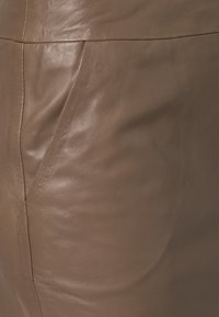 Jupe en cuir marron avec une texture lisse, présentant un design ajusté et une poche discrète sur le côté. Simple avec un minimum de détails.
