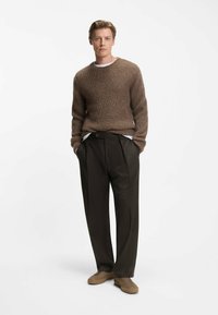 Maglione lavorato a maglia marrone con scollatura rotonda, abbinato a pantaloni scuri plissettati. Sneakers color miele completano il look. Design semplice e moderno.