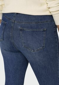 Dark blue denim jeans with a high waist, featuring two back pockets and subtle stitching details. The fabric has a smooth texture.