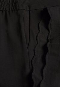 Detailní záběr na černou tkaninu se staženým pasem a vlnkovaným lemem podél švu.