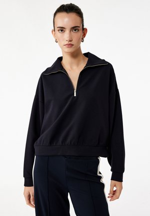 Navy kwart-rits sweatshirt van zacht materiaal met een relaxte pasvorm, geribbelde manchetten en een bandjeszoom. De rits heeft een zilveren trekker.