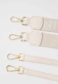 Beige straps with gold hardware, featuring two textured leather ends and a central strap with white lettering.