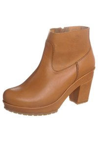 Bota marrón hasta el tobillo con acabado liso, tacón medio en bloque, punta redondeada y detalle de costuras laterales. Presenta un logotipo en la parte exterior del tobillo.