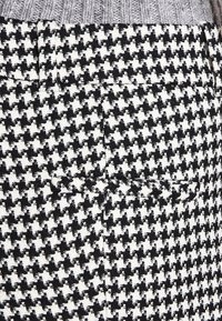 Black and white houndstooth patterned fabric; features stitching details; includes a back pocket with a clean finish.