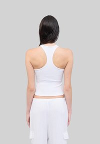 Weißes, geripptes Tanktop mit Racerback-Design, kombiniert mit lockeren, weißen Hosen mit Cargo-Taschen. Glatte Textur, figurbetonte Passform.