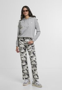 Szara bluza z kapturem z małym logo serca, w połączeniu z jasnymi spodniami cargo w kamuflażu. Sneakersy z szarymi i białymi akcentami dopełniają całość.