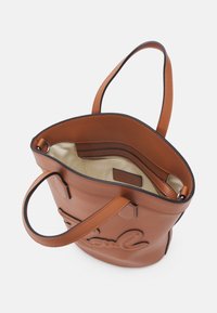 Sac cabas en cuir marron avec deux poignées, intérieur en tissu crème et une poche intérieure zippée.