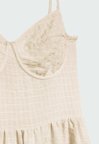 Robe beige avec un motif de grille texturé, dotée d'un corsage ajusté, de bretelles réglables et d'un ourlet volanté. Fabriquée en tissu léger.