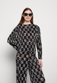 Conjunto padronizado em preto e branco com um corte descontraído, apresentando formas abstratas em tecido pregueado. Acompanhado de óculos de sol redondos pretos.