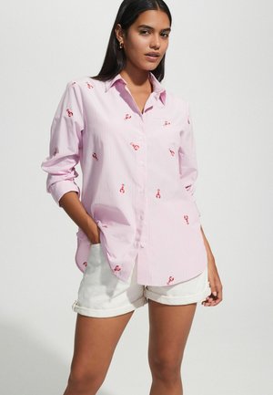 Striped pink button-up shirt featuring red lobster embroidery, long sleeves rolled at the cuffs, paired with white shorts.