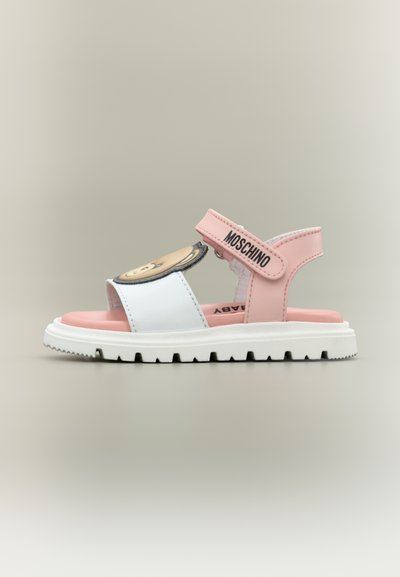 Sandale pour enfant rose et blanche avec un visage d'ours sur la lanière avant et une lanière de cheville rose marquée "Moschino". Semelle blanche rainurée.
