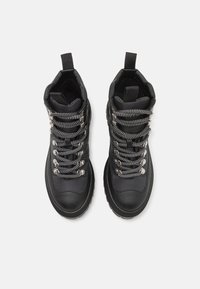 Botas altas negras hechas de cuero texturizado con cordones de patrón en blanco y negro, herrajes plateados y una lengüeta en el cuello.