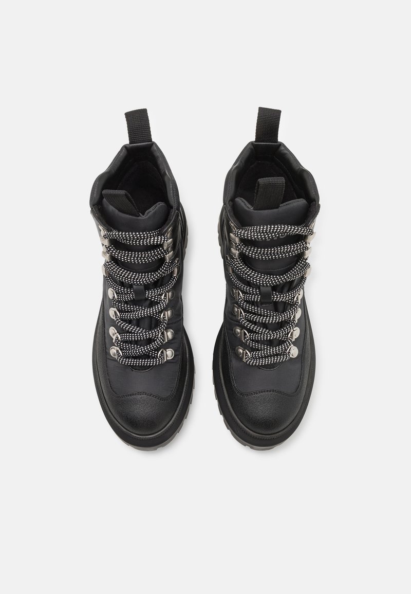 Black high-top boots made of textured leather with black and white patterned laces, silver hardware, and a pull tab on the collar.