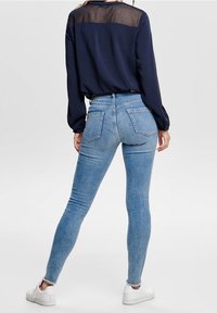 Jeans skinny in denim azzurro chiaro con vita alta, caratterizzati da un design a cinque tasche e un leggero effetto consumato, abbinati a un top blu navy a maniche lunghe.
