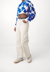 Sudadera corta con patrón floral azul sobre fondo blanco; pantalones vaqueros de tiro alto beige con un ligero acampanado; zapatillas neutras con suelas de goma.