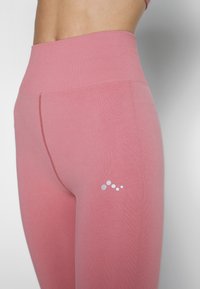 Jasnoróżowe legginsy wykonane z gładkiego, elastycznego materiału z wysokim stanem. Posiadają małe srebrne logo na udzie i minimalne szwy.