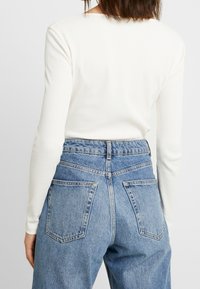 Top bianco a maniche lunghe e a coste abbinato a jeans in denim azzurro chiaro a vita alta con due tasche posteriori e una vestibilità comoda.