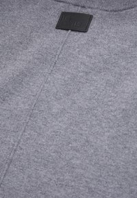 Gros plan d’un tissu tricoté gris avec une couture visible et une petite étiquette noire rectangulaire près de l’encolure.