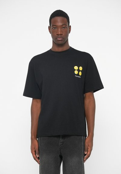 Sort oversized t-shirt lavet af bomuld, med rund halsudskæring, korte ærmer, og gul grafisk design med fire smiley-ansigtter og tekst.