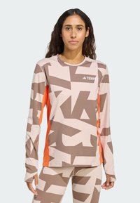 Langärmelig sportief shirt in lichtroze met grote bruine grafische patronen en oranje zijsaccenten. Heeft een ronde halslijn en een gestructureerde stof.