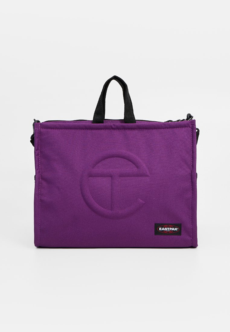 Paarse rechthoekige Eastpak tas met zwarte handvatten, gecentreerd rond het logo, en een ritssluiting aan de bovenkant tegen een plain witte achtergrond.