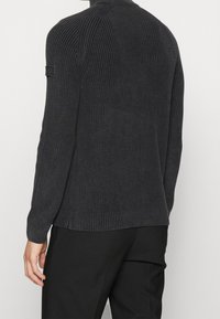 Dzianinowy ciemnoszary sweter o prążkowanej fakturze, z długimi rękawami i dopasowanym krojem. Na lewym ramieniu znajduje się metka.