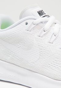 Zapatillas Nike blancas con parte superior de malla, superficie texturizada y cordones planos. Presenta un prominente logo Swoosh blanco y una suela acolchada.