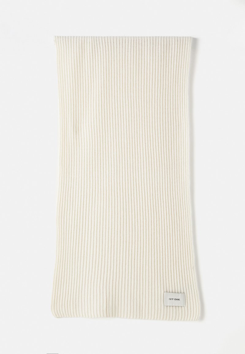 Lyscremet ribbet strikket tørklæde med blød tekstur og rektangulær form. Har et lille grå mærke med "IVY OAK" på siden.
