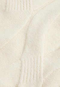 Tejido de punto de crema texturizado con un prominente patrón de zigzag y acentos acanalados. Material suave y grueso con una apariencia cálida y acogedora.