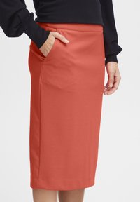 Koraalkleurige kokerrok tot op de knie, gemaakt van rekbaar materiaal, met een zijzak en een gladde textuur. Geschikt voor casual kleding.