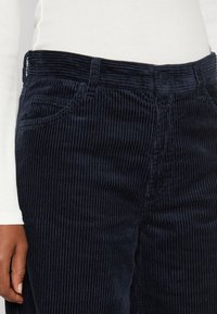 Námořnické manšestrové kalhoty s vertikálním žebrováním, pěti kapsami a prošitými detaily. Pas obsahuje zapínání na knoflík.