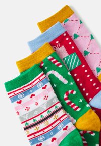 Cuatro pares de calcetines coloridos con patrones festivos: rayas, bastones de caramelo, cajas de regalos y árboles de Navidad. Los materiales parecen suaves y de punto.