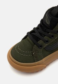 Zapatillas de ante verde con cordones negros, costuras contrastantes y una suela de goma. Presenta un logo en la lengüeta y en el lateral para un detalle de diseño.