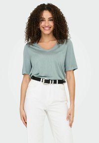 Camiseta de cuello en V color azul claro hecha de una tela suave, combinada con unos jeans blancos de cintura alta y un cinturón negro con hebilla plateada.