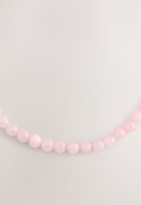 Pink beaded necklace made of smooth, round rose quartz stones, varying in size, strung on a thin thread.