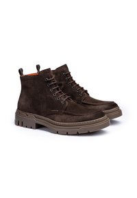 Las botas de tobillo de ante marrón presentan una punta redondeada, una suela de goma marrón contrastante y ojales de metal con cordones a juego. El ante tiene una textura suave.