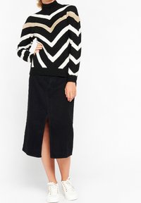 Suéter de patrón de chevrón en blanco y negro con cuello alto, combinado con una falda negra de longitud hasta la rodilla con una abertura frontal y zapatillas blancas.