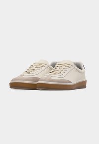 Coppia di sneakers basse color crema con dettagli in suede beige e suole in gomma marrone, mostrati su uno sfondo bianco semplice.