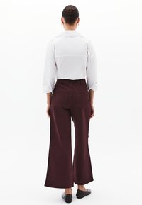 Camicia bianca con maniche arrotolate abbinata a pantaloni ampi bordeaux a vita alta, con tasche posteriori e scarpe nere piatte.