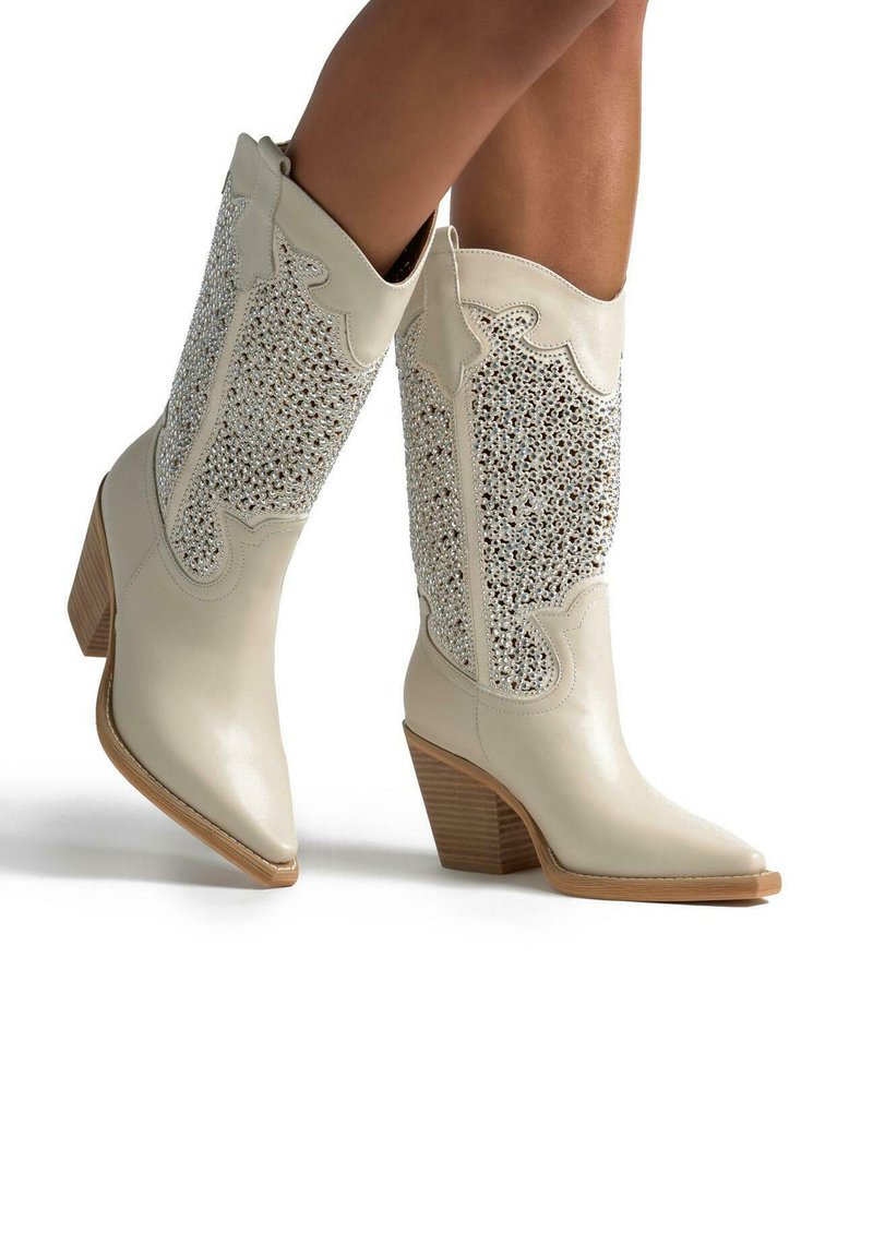Botas de cowboy de cuero blanco con punta afilada, decoradas con piedras de strass en el caña y un tacón cuadrado para estabilidad y soporte.
