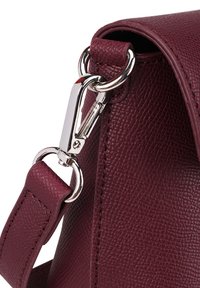 Detail červeného koženého kabelky s texturovaným povrchem, stříbrnými detaily a sponou na popruhu.