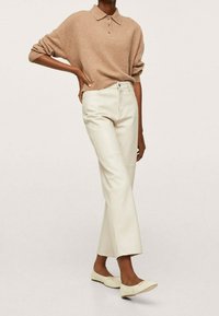Beżowy wełniany sweter polo z trzema guzikami, zestawiony z kremowymi spodniami z ekologicznej skóry oraz jasnymi butami na płaskiej podeszwie.