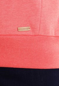 Felpa corallo con orlo a coste e etichetta tessuta con la scritta "radwear". La trama del tessuto è liscia con una finitura morbida.