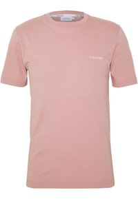Světle růžové bavlněné tričko s krátkými rukávy, kulatým výstřihem a malým bílým logem "Calvin Klein" na hrudi. Měkká textura, volný střih.