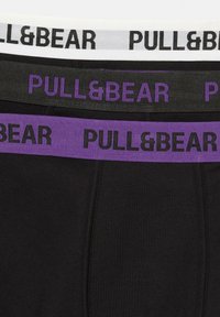 Drie paar zwarte boxershorts met elastische taillebanden in wit, grijs en paars, voorzien van het "PULL&BEAR" logo in contrasterende kleuren.